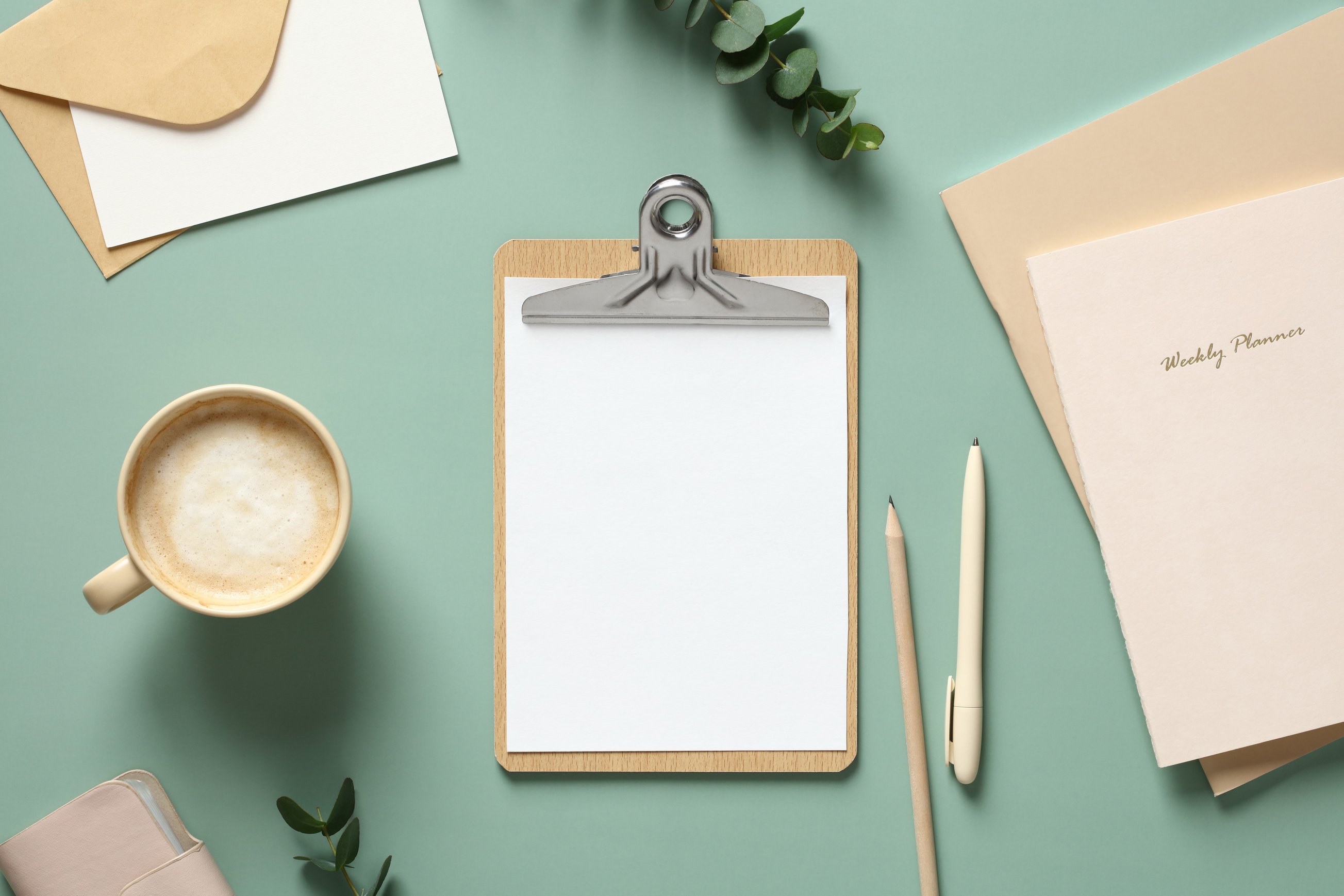 Feminine Workspace with Blank Paper Clipboard on Green Background. Home Office Desk Table with Stationery and Eucalyptus Leaves.